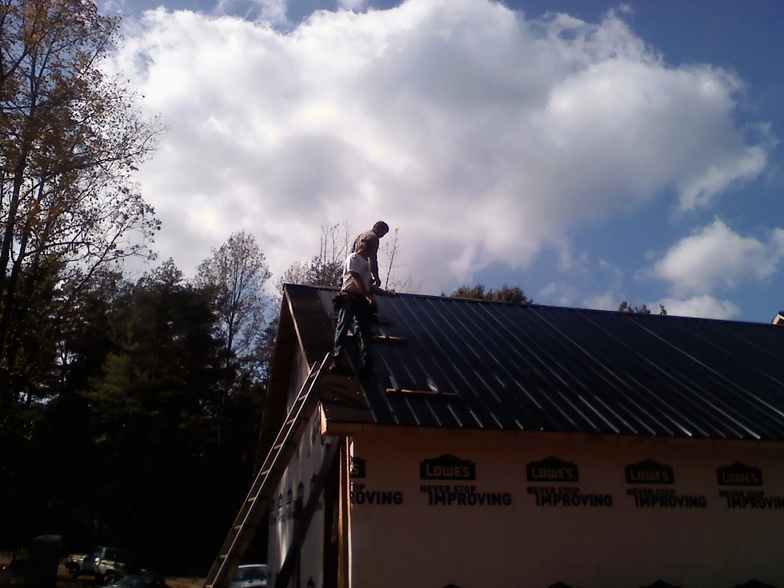 Roofer fastening dark metal panels high against a cloudy sky, from a Roof Inspection job in Camas