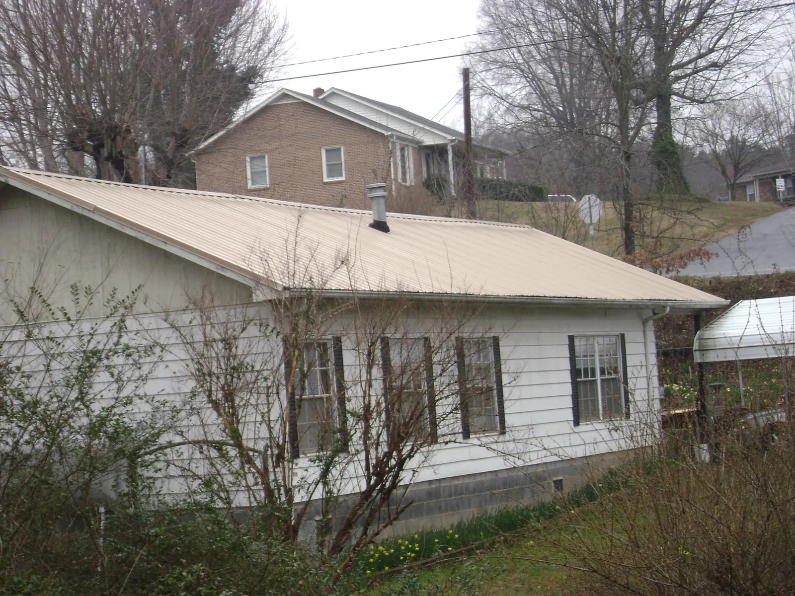 Tan metal roof on a white sided house set into a hillside — Commercial Roofing by Roofing Brothers in Camas